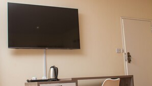 Una habitación compacta con una televisión de pantalla plana montada en la pared, un refrigerador pequeño, un escritorio con una silla y una puerta.