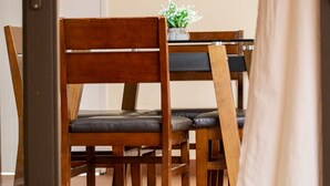 Un comedor con sillas de madera y una mesa, una planta en maceta sobre la mesa, y una puerta al fondo.