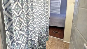 A bathroom with a patterned shower curtain, a window with blinds, and a tiled floor.