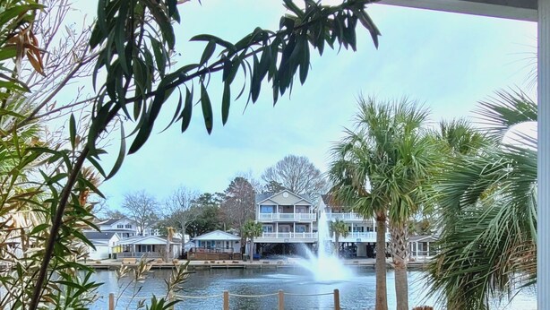 A waterfront view with a building, palm trees, and a fountain.