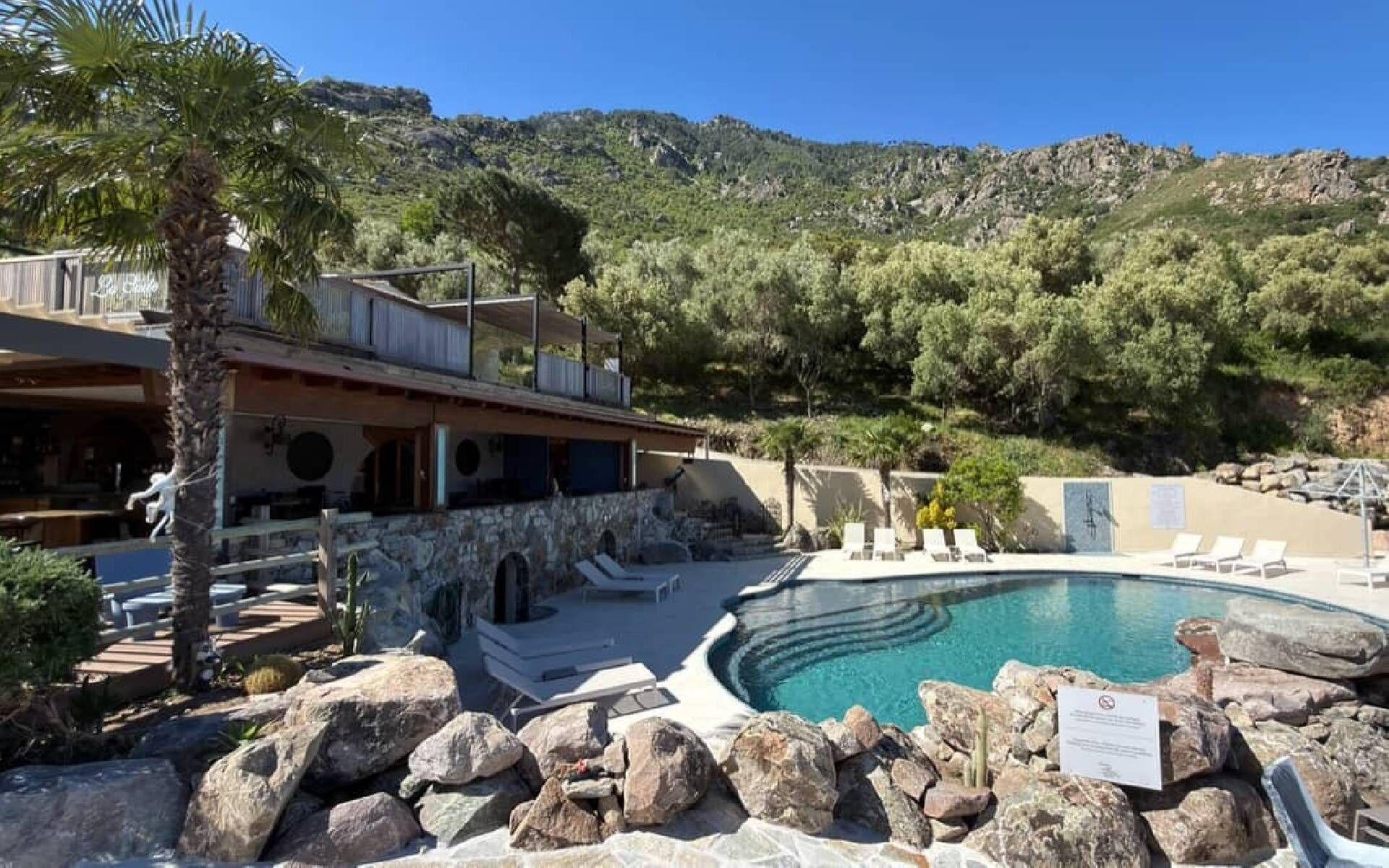 A pool area with lounge chairs, a stone wall, and a mountain backdrop.