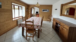 Een eetruimte met een houten tafel en stoelen, een keuken met houten kastjes, en een grote spiegel aan de muur.