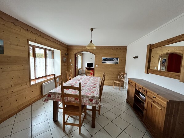 A dining area with a wooden table and chairs, a kitchen with wooden cabinets, and a large mirror on the wall.