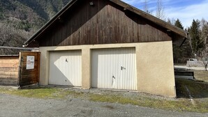 Een tweelaags houten gebouw met een schuin dak en twee witte garagepoorten, met een bord waarop staat dat het een eigendom is genaamd 'Topro'.