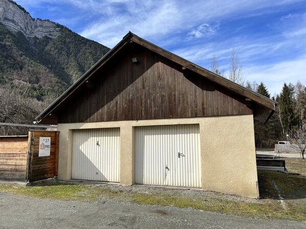 Een tweelaags houten gebouw met een schuin dak en twee witte garagepoorten, met een bord waarop staat dat het een eigendom is genaamd 'Topro'.
