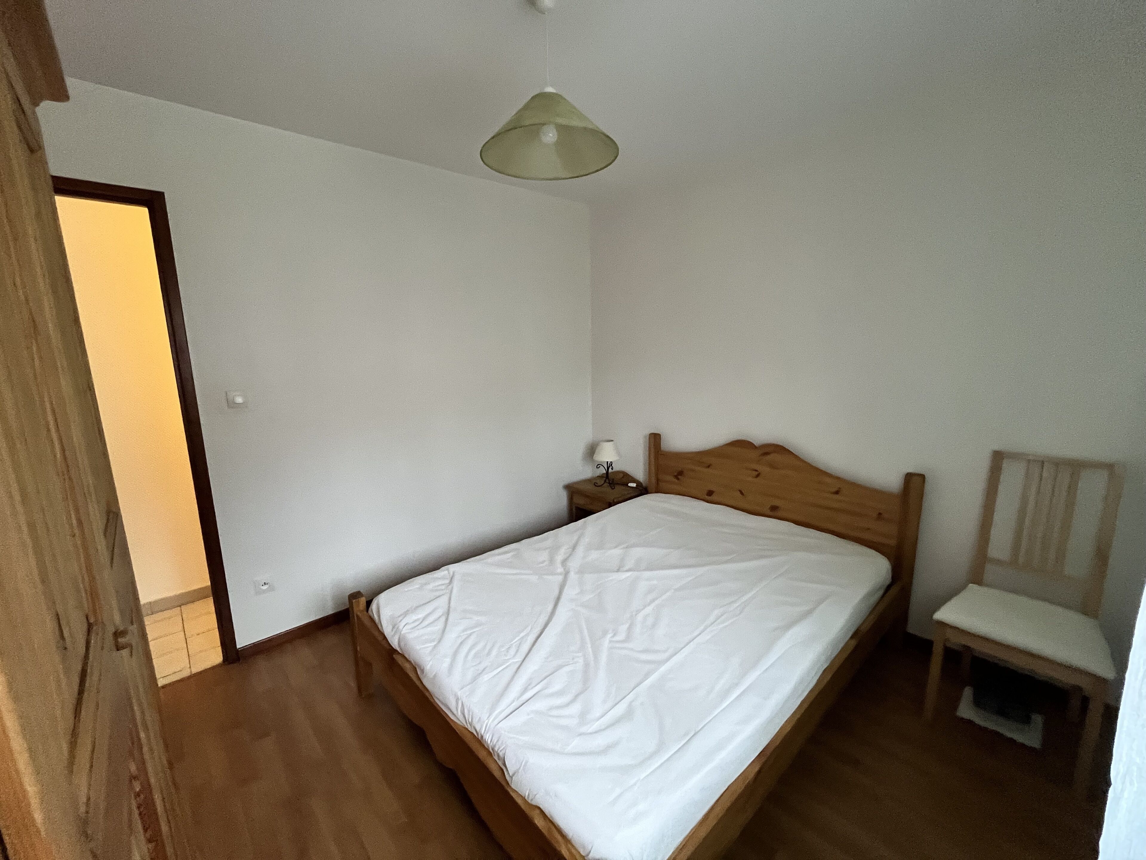 Un dormitorio con una cama de madera, una mesita de noche, una silla y una lámpara colgante.