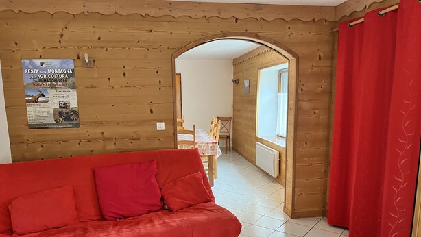 Een kamer met een rode bank, een houten tafel en een poster aan de muur.