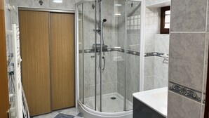Een moderne badkamer met een douchecabine van glas, een houten deur en een witte wastafel.