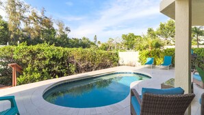 Une piscine à bordures courbes, entourée d’une terrasse aménagée avec des meubles en osier et offrant une vue sur une végétation luxuriante.