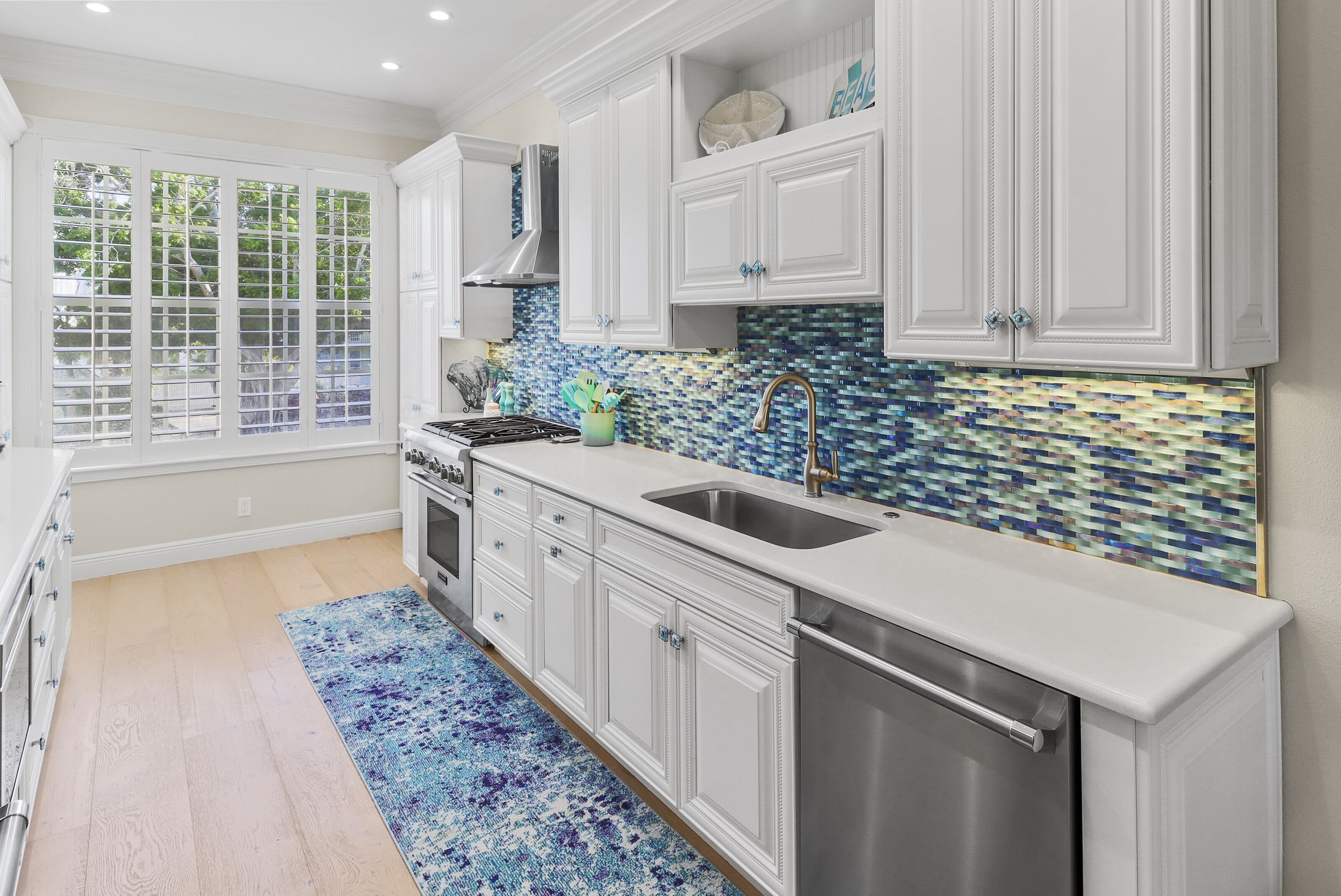 A kitchen with white cabinets, a stainless steel sink, and a blue mosaic backsplash.