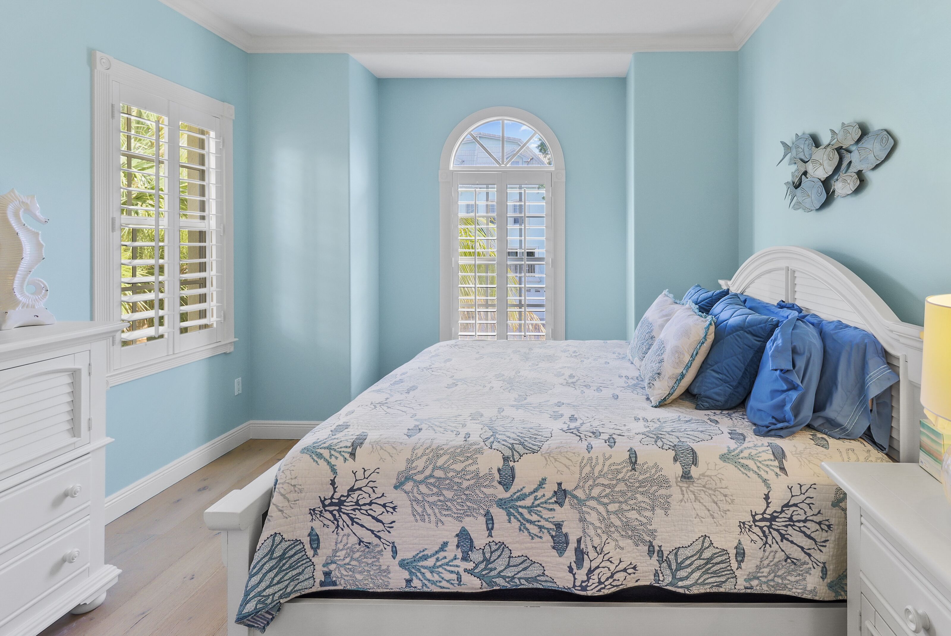 Une chambre à coucher comprenant un lit, une commode, une fenêtre avec des volets et un élément décoratif représentant des poissons, accroché au mur.