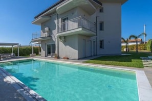 Une maison moderne à deux étages, dotée d’une piscine, d’un balcon et d’une pelouse bien entretenue.