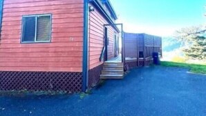 Une cabane en bois rouge, dotée d’un porche et d’un escalier menant à une porte, se dressant sur fond de ciel bleu azur.