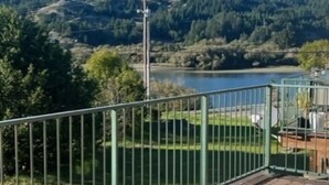 Une terrasse dotée d’une rambarde en métal, qui offre une vue sur un lac et des collines boisées.