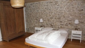 A bedroom with a stone wall, wooden floor, a bed with white bedding, two bedside tables with lamps, and a hanging light fixture.