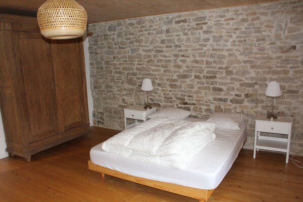 A bedroom with a stone wall, wooden floor, a bed with white bedding, two bedside tables with lamps, and a hanging light fixture. - 4 Bedroom Agritourism property in Les Plains-et-Grands-Essarts (Les Plains-et-Grands-Essarts)