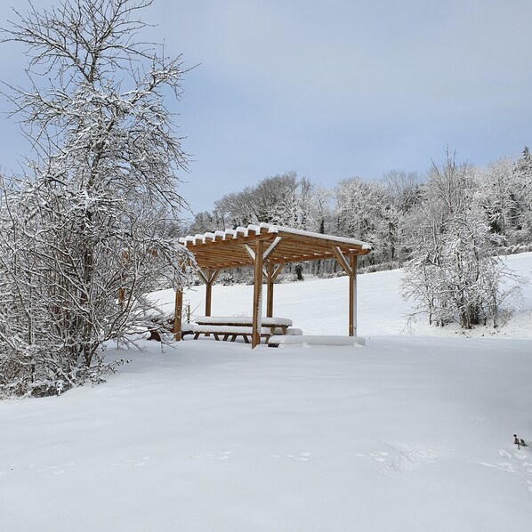 Ein hölzerner Pavillon mit Bänken, umgeben von schneebedeckten Bäumen und einem klaren Himmel.