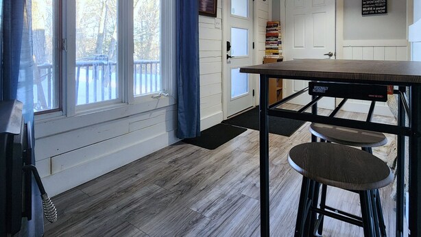 Una cocina con piso de madera, un taburete de bar, una lámpara colgante y una puerta con un letrero.