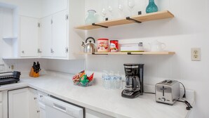 Ett kök med vita skåp, en kaffebryggare, en brödrost och diverse köksredskap på bänkskivan.