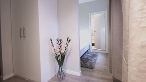 A hallway with a white wardrobe, a vase with flowers, and a door leading to another room. - The APARTMENTS Company - Bislett (Oslo)
