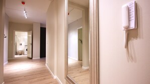 A hallway with a wooden floor, a large mirror, and a telephone mounted on the wall. - The APARTMENTS Company - Bislett (Oslo)