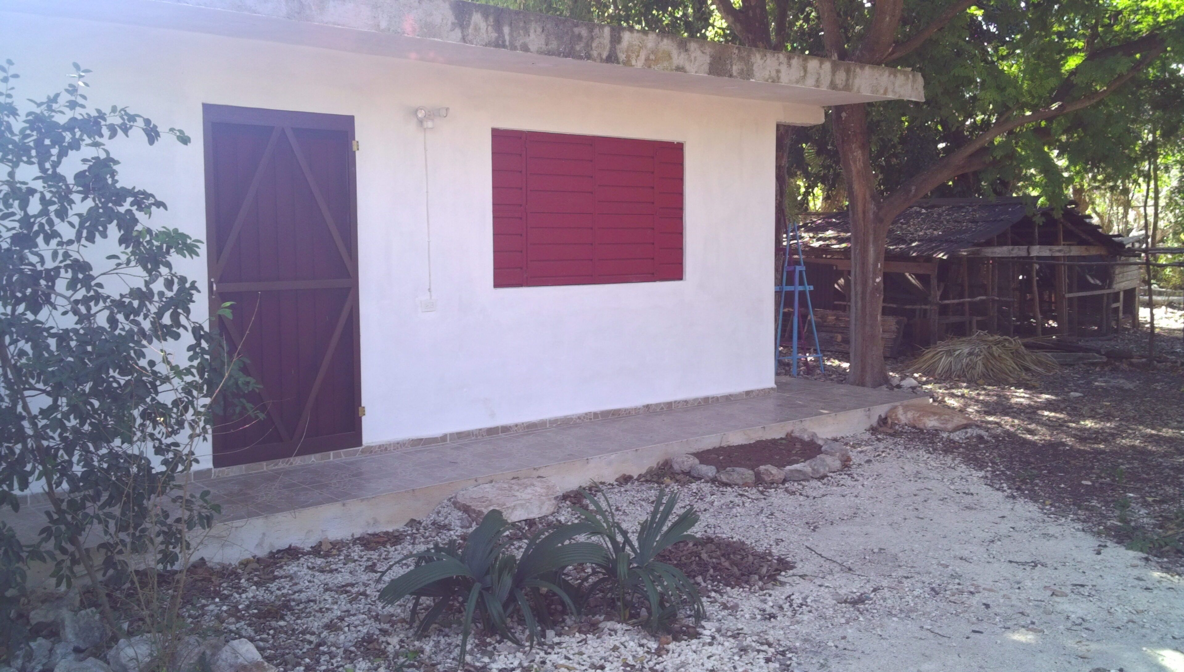 Un pequeño edificio con dos puertas y un persiano rojo.