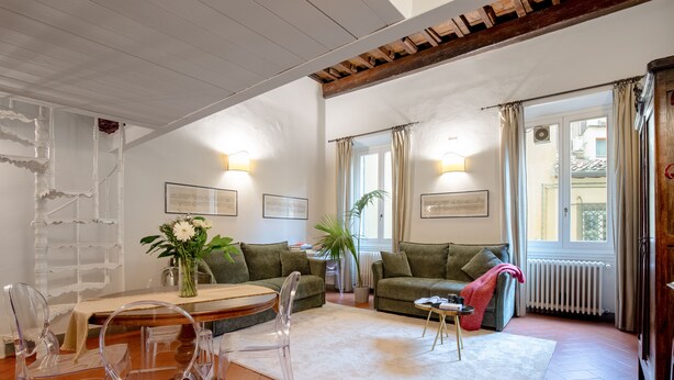 En stue med hvidt loft, træbjælker, et spisebord med stole, en sofa, et sofabord og en radiator.
