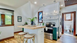 A kitchen with a central island, bar stools, a potted plant, and a view of the outside.