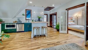 A modern kitchen with a central island, bar stools, and a dining area with a wooden floor.