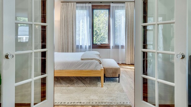 A bedroom with a bed, a bench, and a window with curtains.