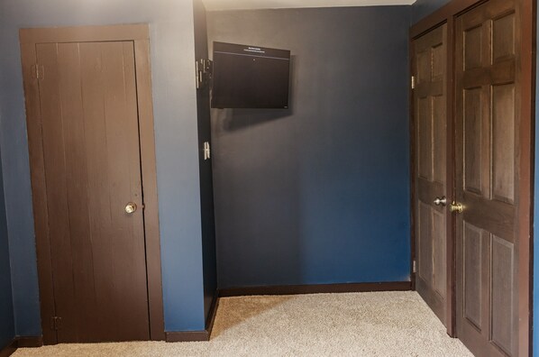 A room with a brown door, a mounted television, and a carpeted floor.