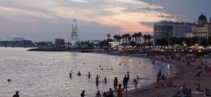 Una playa con gente nadando y tomando el sol, una noria y edificios al fondo.
