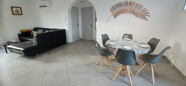 Ein modernes Wohnzimmer mit einer schwarzen Couch, einem Esstisch mit Stühlen und einer Wanddekoration.