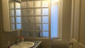 A bathroom with a tiled floor, a sink with a mirror above it, and a window with frosted glass.