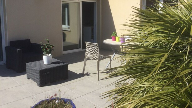 A patio area with a sofa, a small table with potted plants, and a chair.