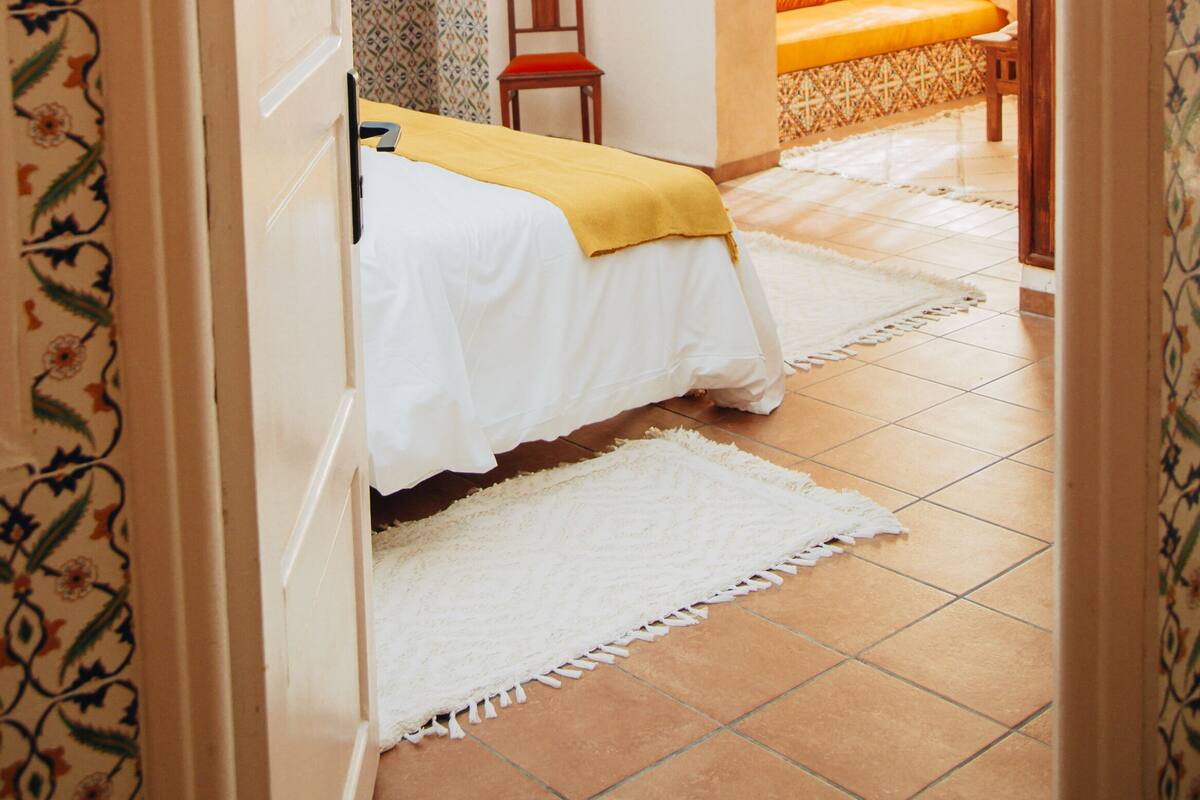 Una habitación con una cama, una silla, un televisor y una lámpara de fibra natural.