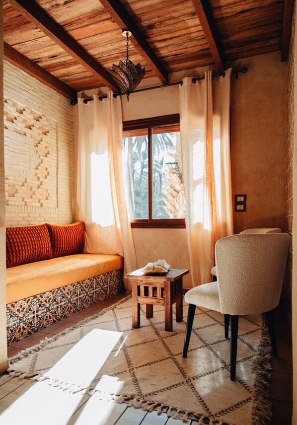 A cozy room with a wooden ceiling, a patterned sofa, a small table, and a chair. - DAR EBBA  (Degache)