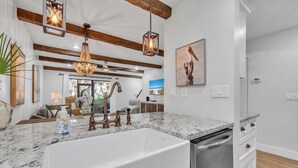A modern kitchen with a large white sink, stainless steel dishwasher, and marble countertops.