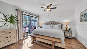 A bedroom with a bed, bedside tables, a bench, a ceiling fan, and a view through a glass door.