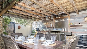 An outdoor kitchen with a stone wall, wooden ceiling, and wicker furniture.