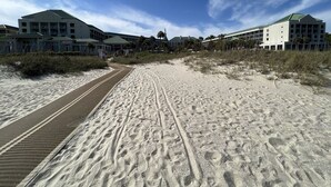 Una playa arenosa con un paseo marítimo que conduce a edificios con techos verdes.