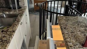 A kitchen with white cabinets, a granite countertop, and a black metal staircase. - The Escape Pod @Cheat Lake, private Hot Tub, near WVU (Morgantown)