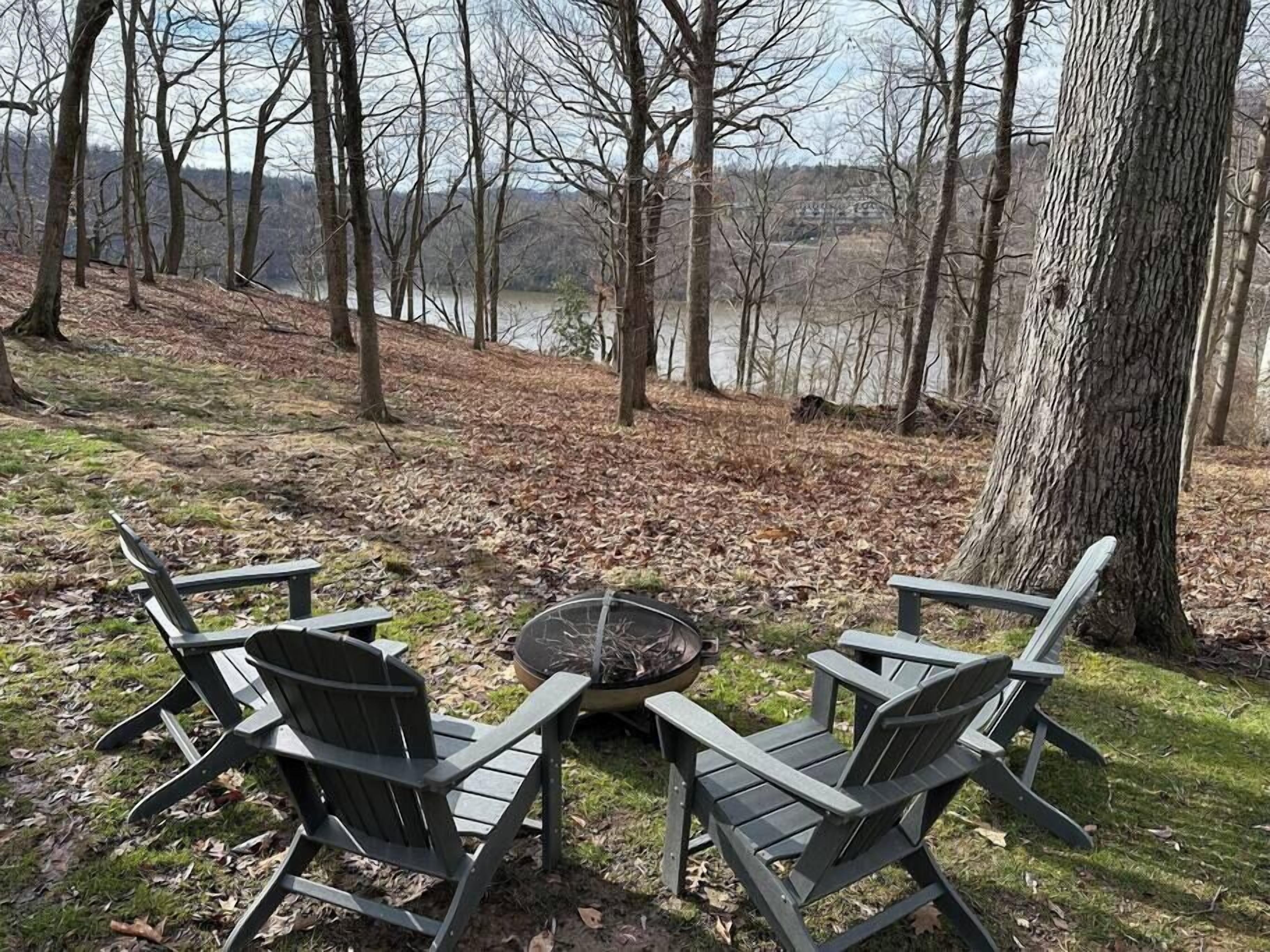 Vista de una zona junto al lago con una hoguera y sillas Adirondack.