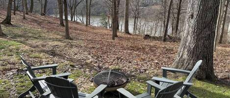 Vista de una zona junto al lago con una hoguera y sillas Adirondack.
