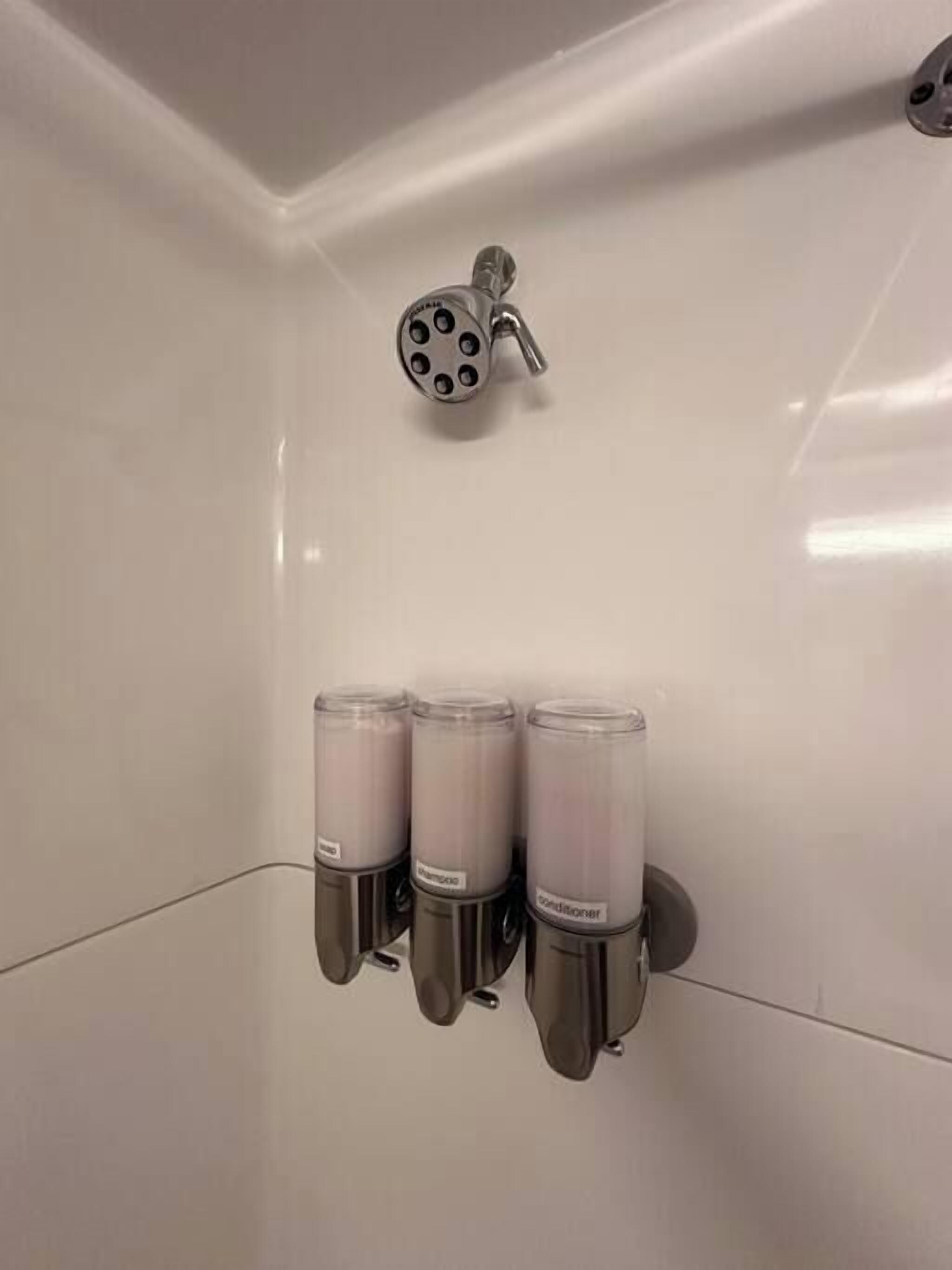 Ein Badezimmer mit Duschkopf und drei Spendern an der Wand.