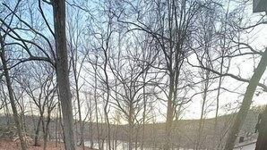 A wooden deck with outdoor furniture, a staircase, and a view of trees and a body of water. - The Escape Pod @Cheat Lake, private Hot Tub, near WVU (Morgantown)