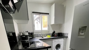A compact kitchen with a washing machine, a coffee maker, and a refrigerator.