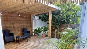 A wooden deck with two chairs and a table, surrounded by potted plants and a wooden fence.