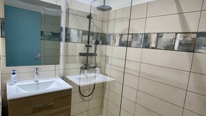 A modern bathroom with a glass-enclosed shower, a vanity with a sink, and a mirror.