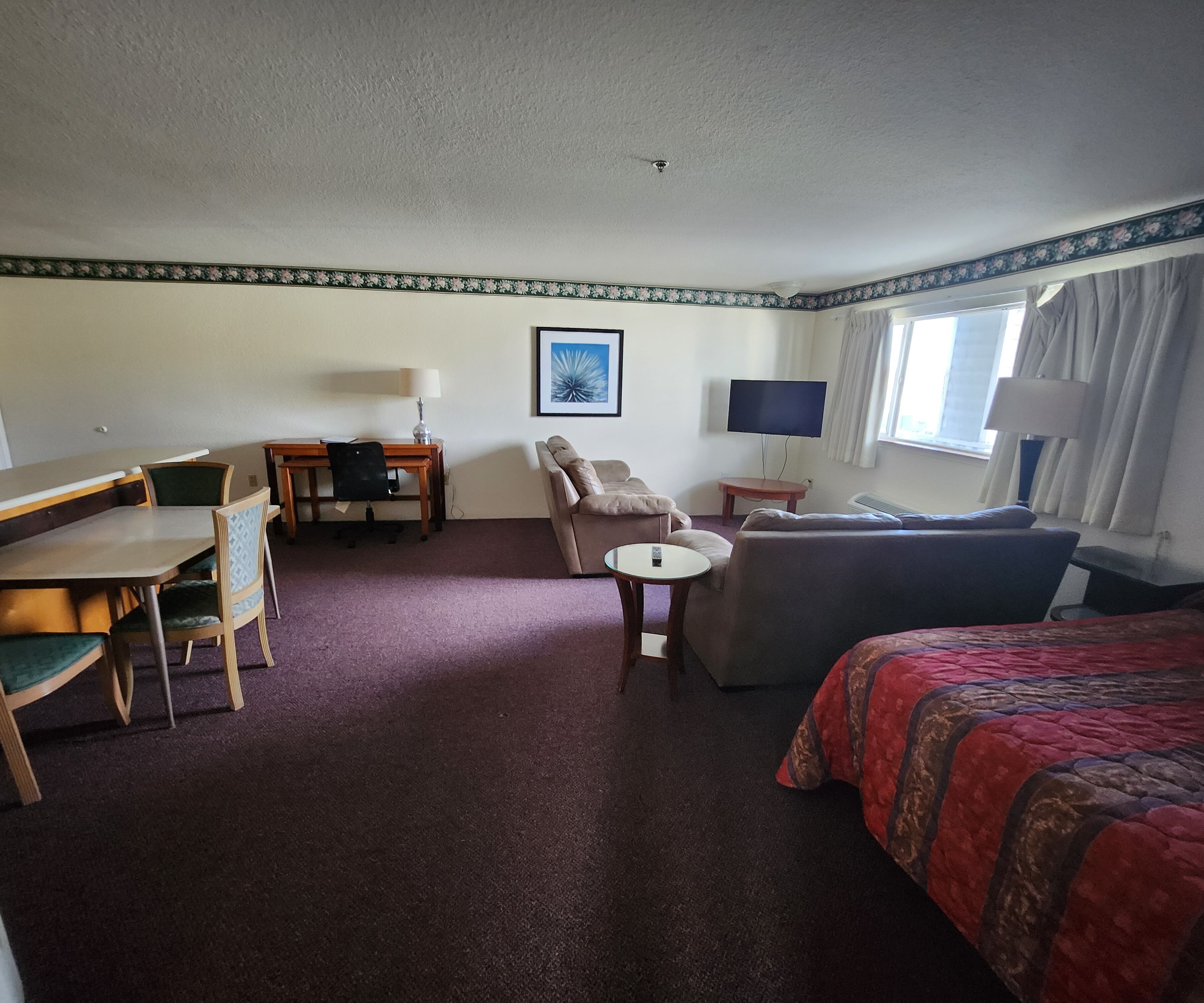A hotel room with a bed, a sofa, a desk, a chair, a small table, a TV, and a window with curtains.